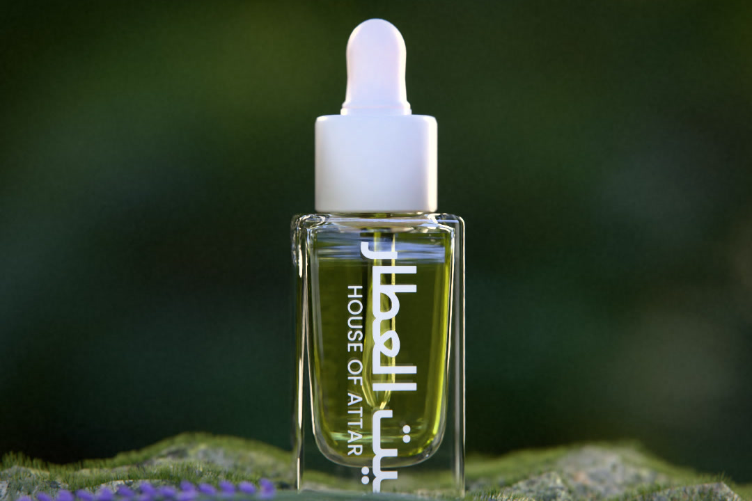 A House of Attar glass dropper bottle of perfume oil on moss beside lavender